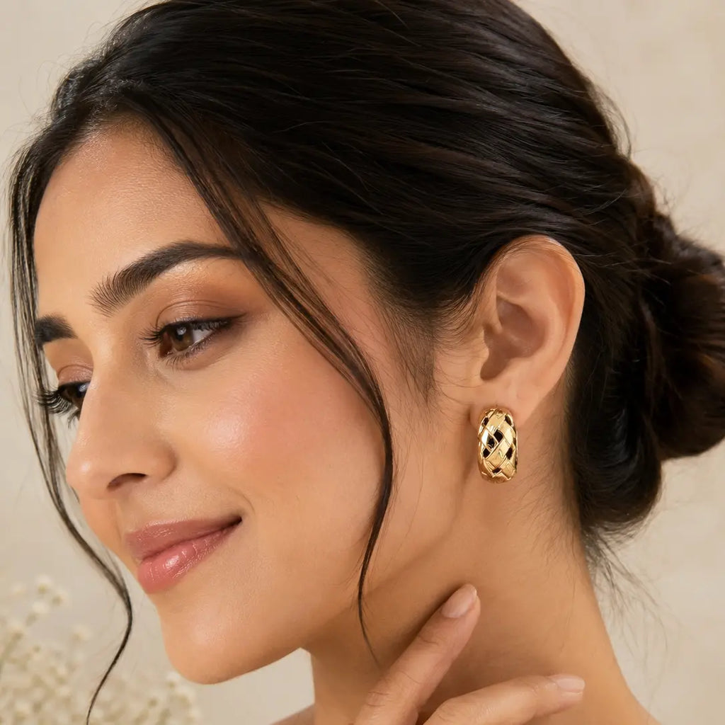 Elegant woman wearing EVAH JEWELS gold-tone chunky woven hoop earrings featuring a polished interlocking braided design, textured lattice detailing and a bold statement style, beautifully showcased with a sophisticated low-bun hairstyle.