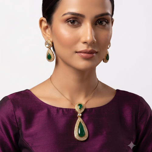 EVAH JEWELS emerald green teardrop pendant necklace and matching drop earrings worn by a woman in a maroon outfit, featuring gold-tone settings and sparkling white stones.