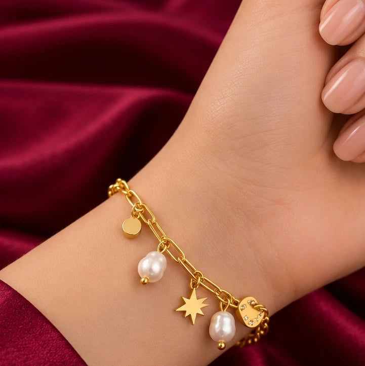 Add a touch of elegance and charm to your everyday style with the EVAH JEWELS Gold Tone Heart and Pearl Charm Bracelet for Women, a beautifully designed fashion jewellery accessory featuring a delicate gold-tone chain link bracelet adorned with graceful pearl-style drops, a sparkling stone-studded heart charm, a stylish star charm and a polished round gold-tone charm. Beautifully showcased on a model's wrist against a luxurious burgundy satin background, this elegant bracelet highlights its feminine detaili