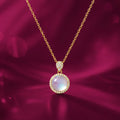 Elegant gold-plated moonstone halo pendant necklace by EVAH JEWELS, featuring a round iridescent moonstone-style centerpiece surrounded by sparkling CZ stones, a delicate gold chain and a luxurious pink background. Stylish fashion jewellery for women, perfect for everyday wear, parties and gifting.