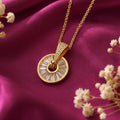 Elegant gold plated Sunburst Wheel Pendant Necklace for Women featuring a circular design with sparkling baguette-cut stones and a crystal-studded bail, displayed on luxurious pink satin fabric. Shop stylish anti-tarnish fashion jewellery online in India at EVAH JEWELS.