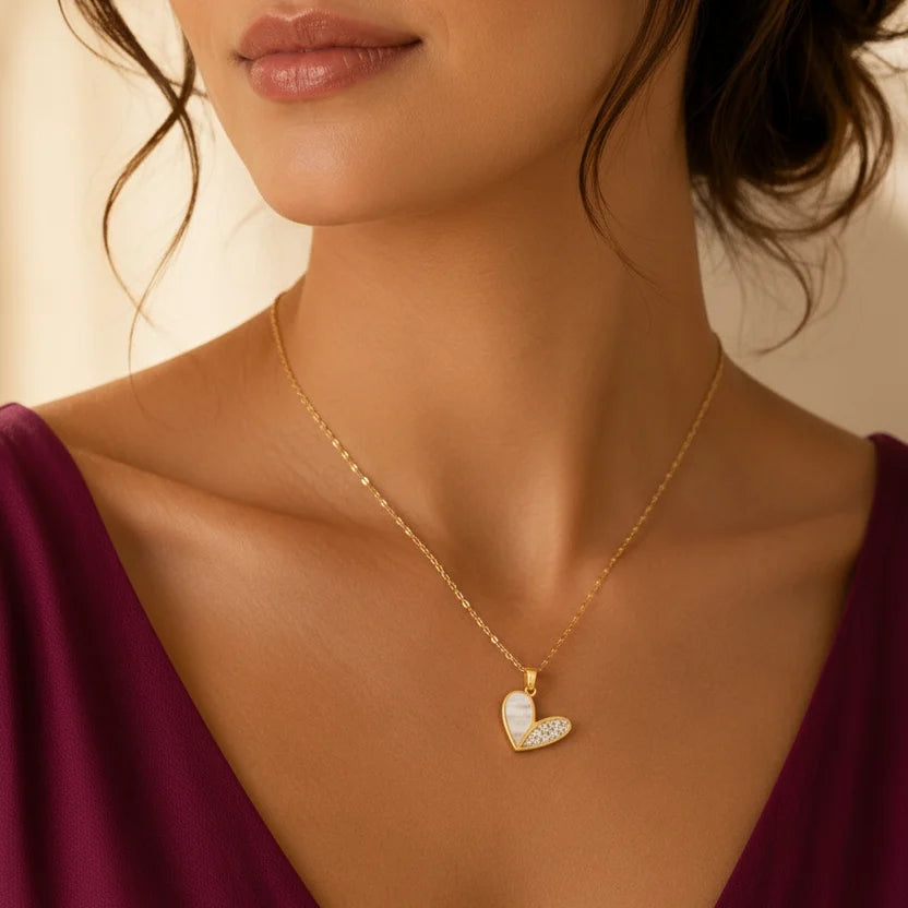 Woman wearing EVAH JEWELS gold-plated half pavé mother of pearl heart pendant necklace, featuring a sparkling crystal-studded heart design, elegant white mother of pearl inlay and delicate gold-tone chain, styled with a burgundy dress.