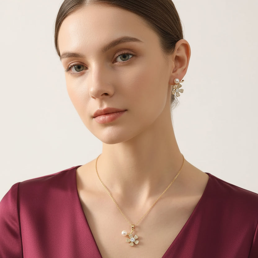 Woman wearing EVAH JEWELS gold-tone floral pendant necklace and matching flower earrings with sparkling crystal petals and white pearl accents, styled with a burgundy dress.