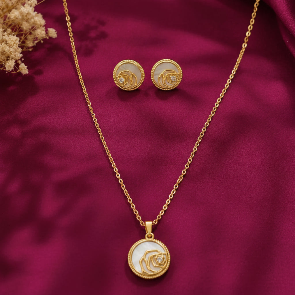 gold-tone floral pendant necklace and matching stud earrings set for women, featuring round white enamel-style detailing, delicate rose designs and sparkling crystal accents on burgundy satin by Evah Jewels.
