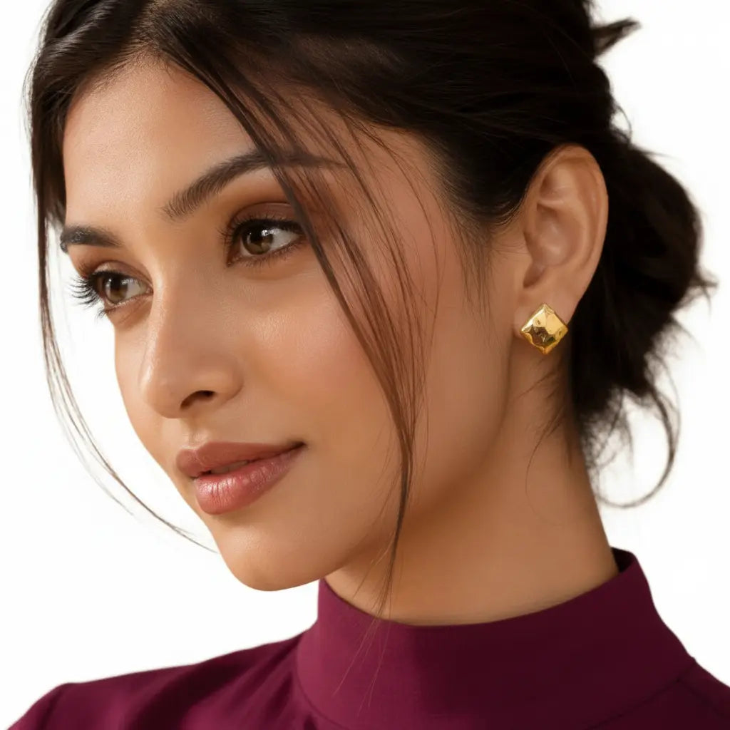 Elegant woman wearing EVAH JEWELS gold-tone geometric diamond-shaped stud earrings featuring a polished faceted design and modern minimalist styling, paired with a burgundy high-neck outfit and elegant updo against a white background.