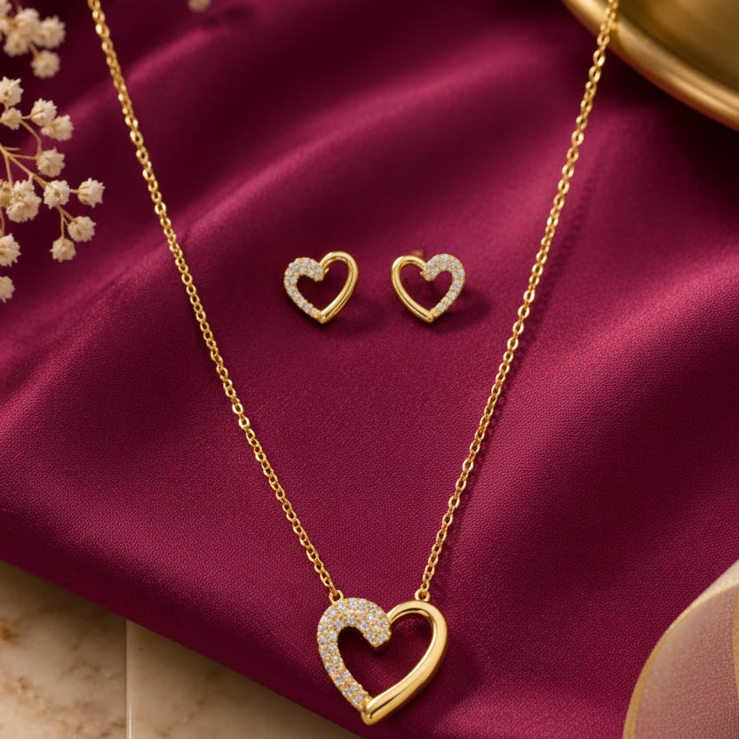 gold-tone heart pendant necklace and matching heart stud earrings for women, featuring sparkling crystal accents and an open-heart design on burgundy satin by Evah Jewels.