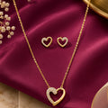 gold-tone heart pendant necklace and matching heart stud earrings for women, featuring sparkling crystal accents and an open-heart design on burgundy satin by Evah Jewels.