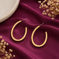minimalist gold-tone oval hoop earrings for women featuring a sleek open-hoop design and polished finish, displayed on burgundy satin with delicate dried flowers by Evah Jewels.