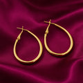 classic gold-tone oval hoop earrings for women featuring a smooth polished finish, elegant lightweight-looking design and secure hinged closures, beautifully displayed on luxurious burgundy satin fabric by Evah Jewels.