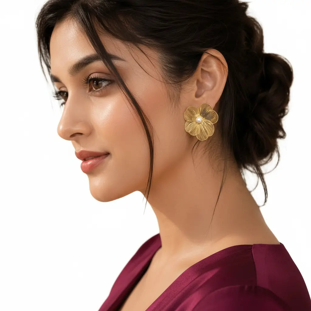 Elegant woman wearing EVAH JEWELS gold-tone floral pearl statement stud earrings featuring five intricately textured flower petals and a delicate white pearl centre, styled with a sophisticated low bun and burgundy outfit against a white background.