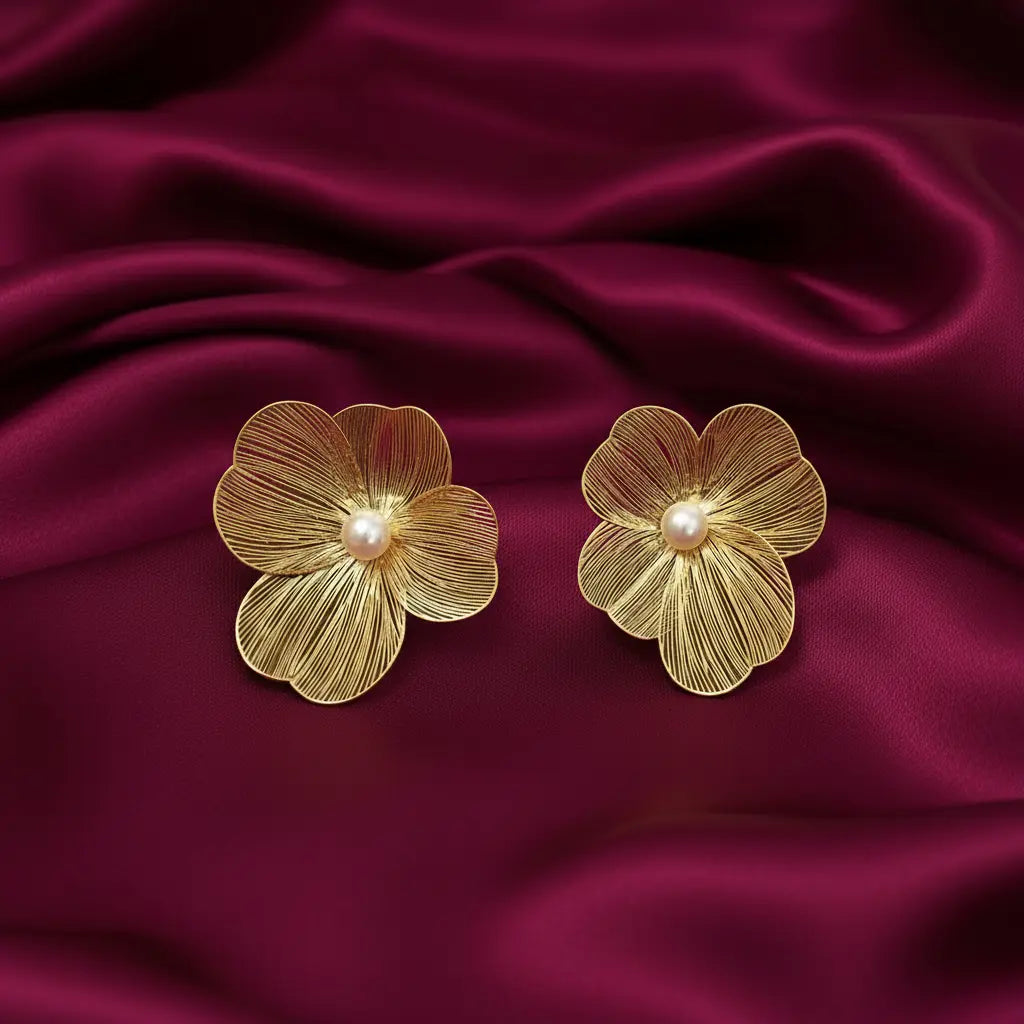 gold-tone floral pearl statement stud earrings for women featuring five textured flower petals, delicate engraved vein detailing and elegant round white pearl centres, displayed on luxurious burgundy satin fabric by Evah Jewels.