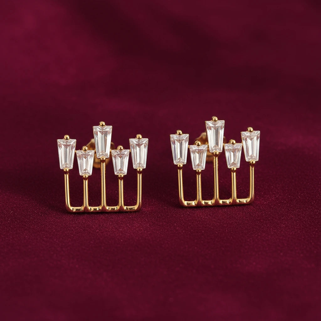 gold-tone geometric baguette crystal stud earrings for women featuring five sparkling rectangular clear stones arranged at varying heights in an elegant open-frame design, displayed on luxurious burgundy velvet fabric by Evah Jewels.
