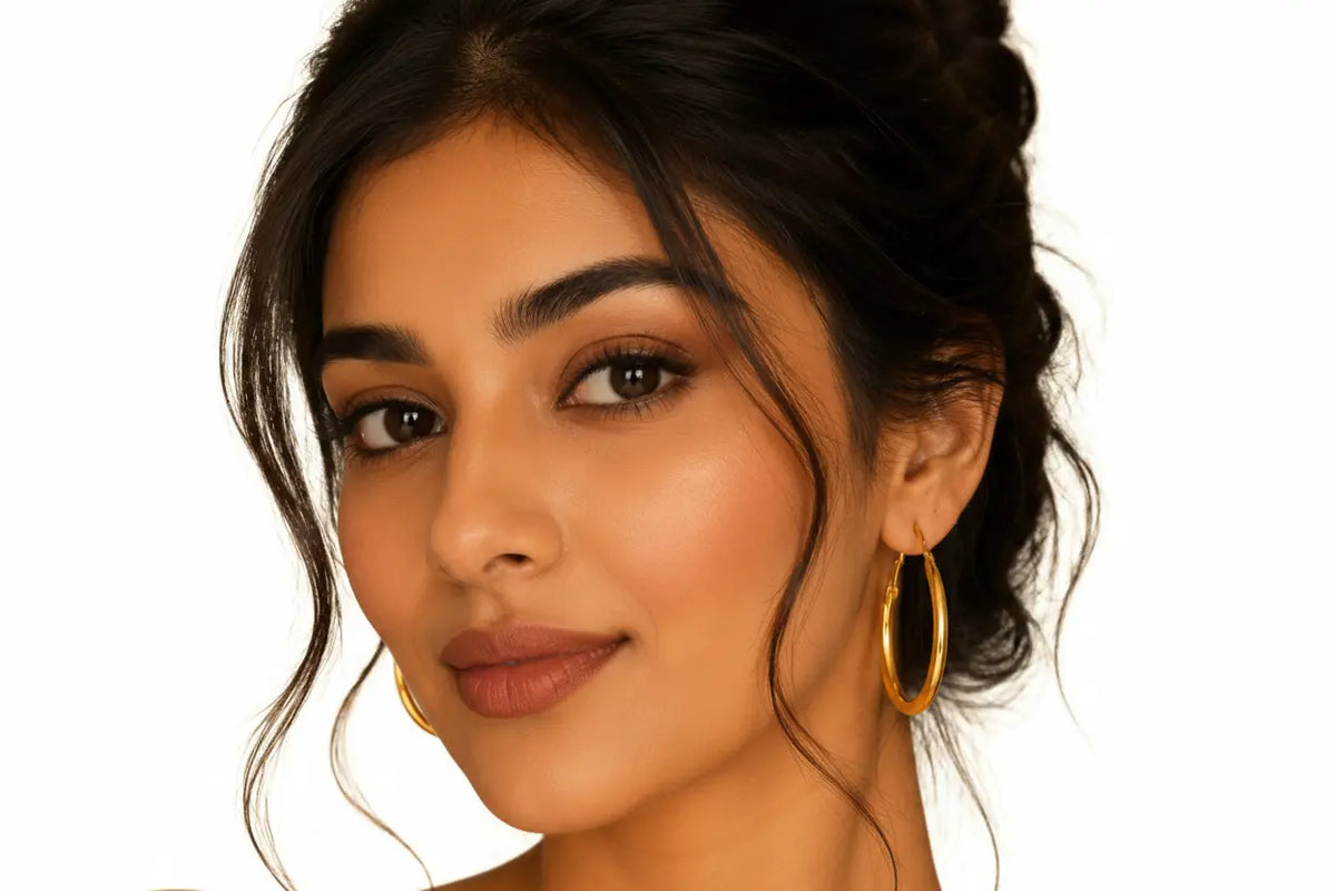 Elegant woman wearing EVAH JEWELS classic gold-tone oval hoop earrings featuring a smooth polished finish and minimalist elongated design, styled with a sophisticated updo against a clean white background.
