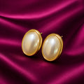 gold-plated oval pearl stud earrings for women featuring lustrous white pearl centres, polished gold-tone borders and a classic minimalist design, displayed on luxurious burgundy satin fabric by Evah Jewels.