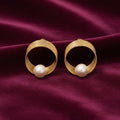 gold-tone circular spiral pearl stud earrings for women featuring layered concentric wire loops, an elegant open-circle geometric design and luminous round white pearl accents, displayed on luxurious burgundy satin fabricby Evah Jewels.