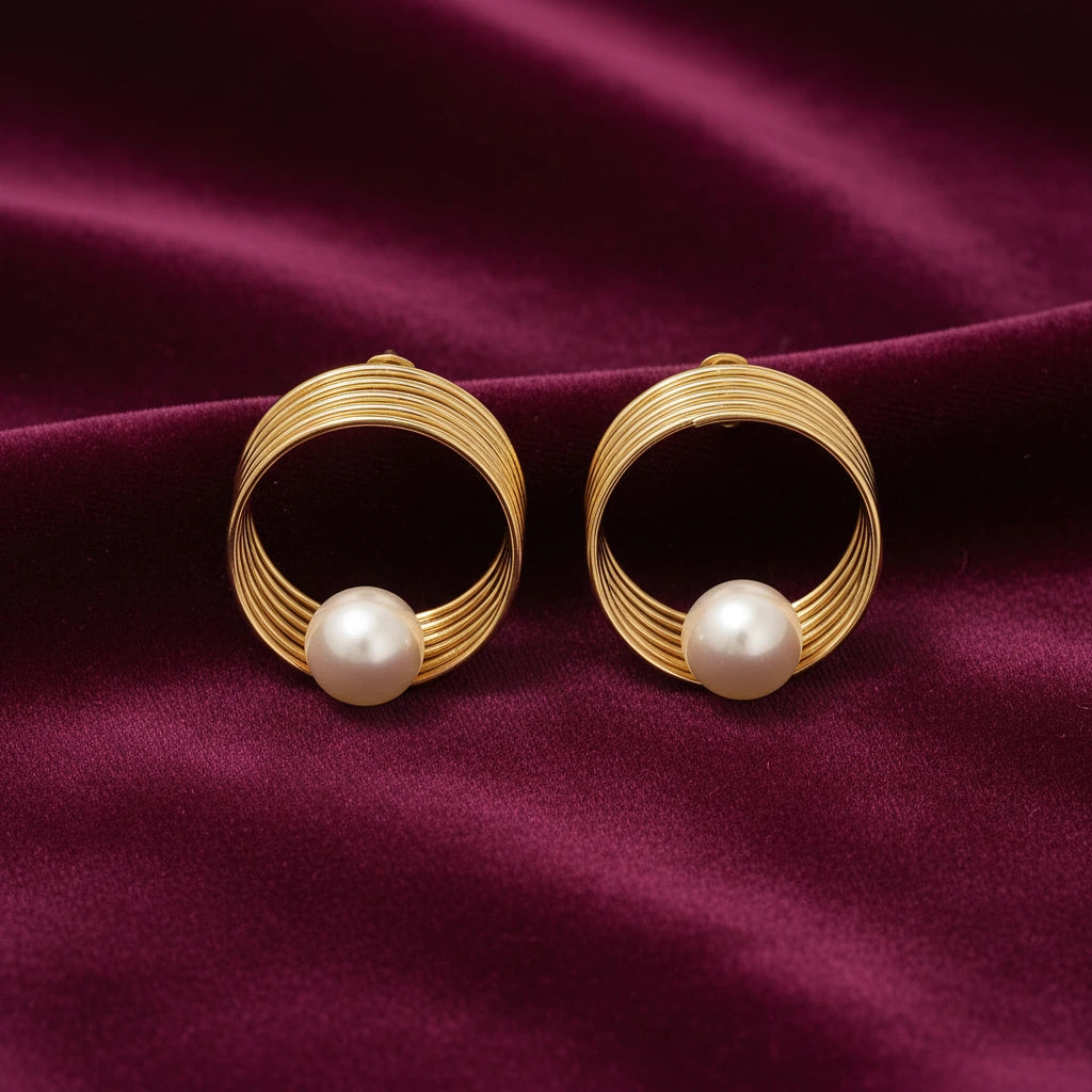gold-tone circular spiral pearl stud earrings for women featuring layered concentric wire loops, an elegant open-circle geometric design and luminous round white pearl accents, displayed on luxurious burgundy satin fabricby Evah Jewels.