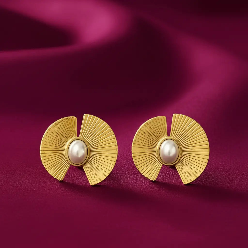 gold-tone sunburst pearl statement stud earrings for women featuring elegant oval white pearl centres, textured fan-shaped geometric detailing and a radiant gold finish, displayed on luxurious burgundy satin fabric by Evah Jewls.