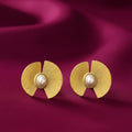 gold-tone sunburst pearl statement stud earrings for women featuring elegant oval white pearl centres, textured fan-shaped geometric detailing and a radiant gold finish, displayed on luxurious burgundy satin fabric by Evah Jewls.