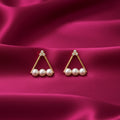 gold-tone triangular pearl stud earrings for women featuring three lustrous white pearls, sparkling crystal-studded floral accents and a delicate geometric design, displayed on luxurious pink satin fabric by Evah Jewels.