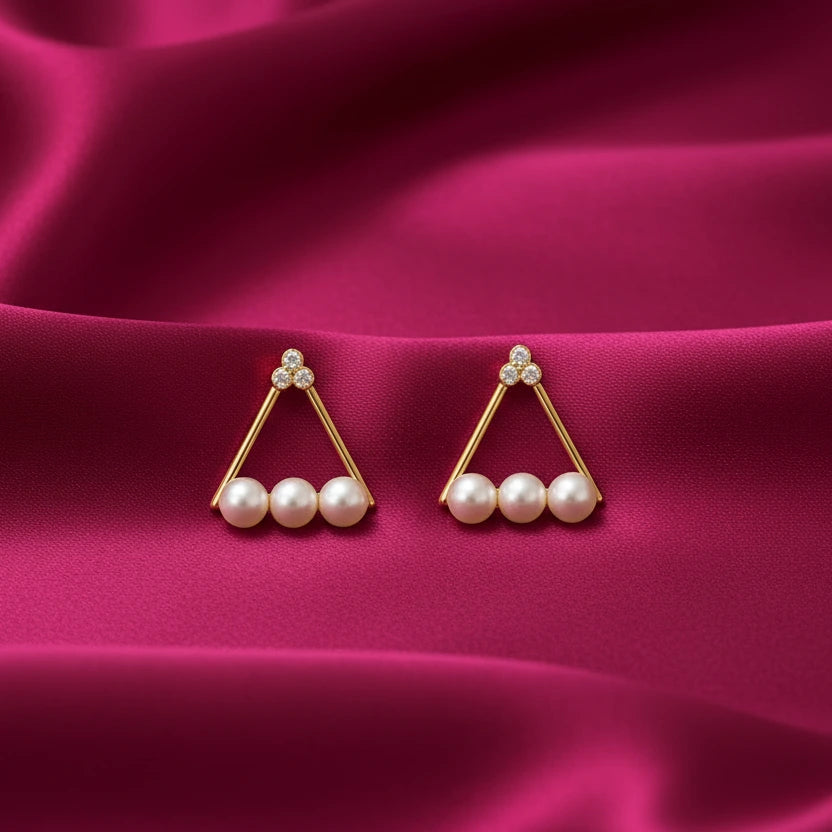 gold-tone triangular pearl stud earrings for women featuring three lustrous white pearls, sparkling crystal-studded floral accents and a delicate geometric design, displayed on luxurious pink satin fabric by Evah Jewels.