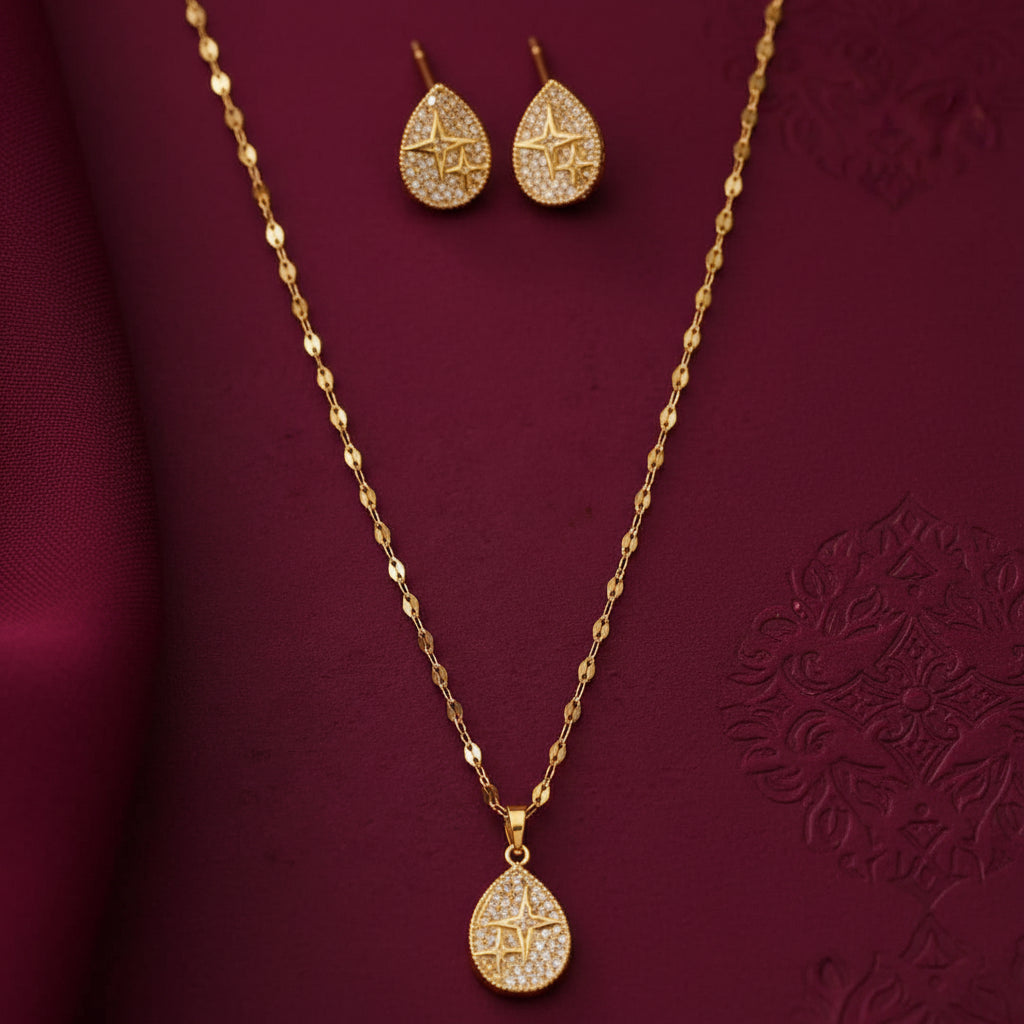 gold-tone teardrop pendant necklace and matching stud earrings set for women, featuring sparkling crystal-like stones and geometric star designs on a burgundy background by Evah Jewels.