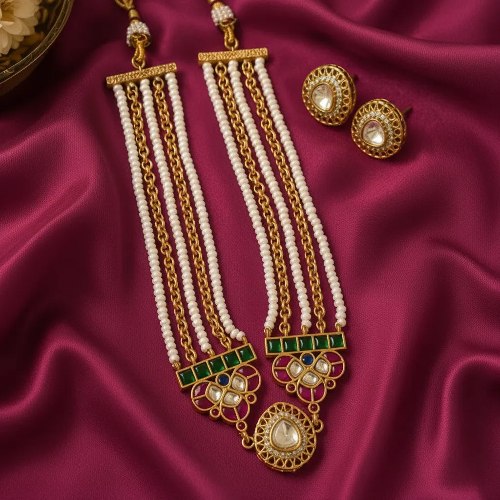 traditional gold-tone Kundan pearl necklace set for women featuring multiple white pearl bead strands, gold chains, rectangular green stone accents, intricate pink and white stone floral motifs, and a teardrop-shaped Kundan pendant with matching gold-tone stud earrings, displayed on luxurious burgundy satin fabric. Elegant Indian ethnic jewellery for weddings, festive occasions and traditional celebrations by Evah Jewels.

