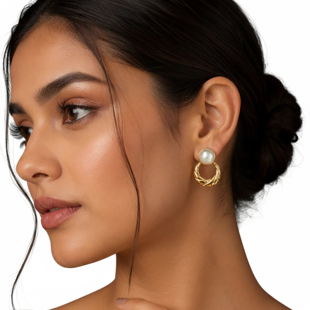 Elegant woman wearing EVAH JEWELS gold-tone pearl twisted hoop drop earrings featuring lustrous round white pearl-like studs and textured gold circular drops, styled with a sophisticated low bun against a white background.