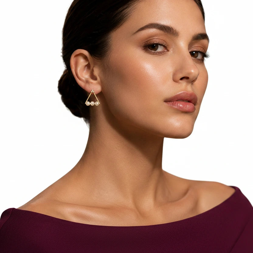Elegant woman wearing EVAH JEWELS gold-tone triangular pearl stud earrings featuring three lustrous white pearl accents, a sparkling crystal-studded top and minimalist geometric design, styled with a burgundy off-shoulder dress.